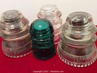 Front view showing four glass electrical insulators in a row, three clear and one blue-green.
