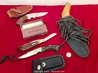 Photo showing three folding knives, sheaths, and a penny for scale on red background.