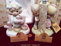 Two Precious Moments figurines with their original styrofoam and boxes in the background; a quarter placed for scale.