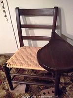 Front view of dark wooden chair with woven seat, showing side arm rest/tray on right side.