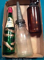 Photo showing all three bottles inside a cardboard tray: clear bottle with metal pump, green wine bottle with monkey arms, and plain brown bottle.