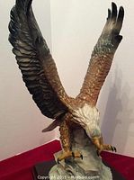 Eagle sculpture with wings extended, showing detailed paint and base, positioned against red backdrop