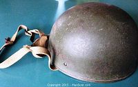 Profile view of the olive green military helmet showing the outer metal shell and head strap.
