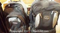 Two assorted backpacks: one primarily black with gray panels and zipped compartments, the other black with a circular logo patch visible on the front pocket.