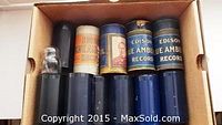 Box containing twelve cylindrical phonograph rolls including four with Edison Blue Amberol labels and others with various Victrola labels in cardboard and protective sleeves.