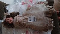 Full view of the antique bride doll dressed in a lace bridal gown, lying down.