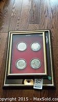 Full view of one shadow box with four metal decor pieces each with a coin in the middle placed on a red background and gold-tone frame.