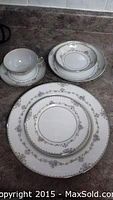 Photo of stacked plates, bowls and cups showing silver floral rim pattern on white china.