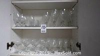 Shelf showing clear glass stemmed glasses and various other glassware in cabinet