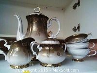 Photo showing tea pot, creamer, sugar bowl, stacked cups and saucers on a shelf.