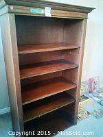 Front view of one walnut finish wooden bookcase showing four shelves and decorative molding on top.