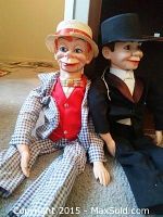 Two ventriloquist dummies seated on carpet, showing full bodies and attire.