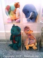 Twelve Beanie Babies plush toys individually enclosed in clear plastic display cases. Various animals including colorful elephant, dolphin, bear, duck, fish, butterfly, rabbit, and unicorn are visible.
