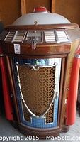 Full front view of Seeburg jukebox showing wood veneer front, red side columns, chrome grille and coin slot area