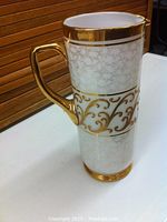 Side view of tall Bohemia glass vase showing embossed gold floral design on frosted white glass, gold handle and rim