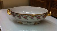 Full side view of white porcelain serving bowl with floral Bridal Wreath pattern and gold gilded handles and footed base.