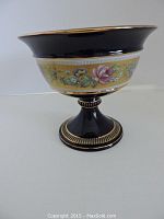 Front view of dark blue pedestal bowl showing floral pattern and gold trim.