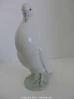 Front side view of the large white dove figurine on a greenish base against white background.