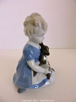 Porcelain figurine side view showing the girl holding a dark brown fawn while sitting, wearing a blue dress.