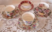 Four teacup and saucer sets with floral and gold detailing on lace cloth.