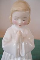 Close-up of the figurine's face and clasped hands showing delicate features and gloss finish.