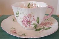 Side view of Shelley fine bone china teacup and saucer with pink trimmed scalloped edges, pink handle, and pink floral print.