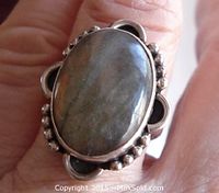 Close-up front view of oval labradorite cabochon set in oxidized sterling silver ring on finger.