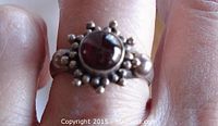 Front view of sterling silver ring with round garnet cabochon stone and decorative beaded silver detail around stone.
