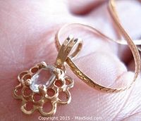 Close-up of the small 10K gold pendant with oval aquamarine gemstone in a floral openwork design showing prong setting and bail.