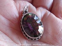 Close-up of the front face of the oval facetted mystic topaz pendant held in hand, showing the rainbow colors and silver bezel setting.