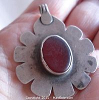 Front view of old sterling silver pendant with bezel-set oval carnelian stone, showing scalloped petal design edges.