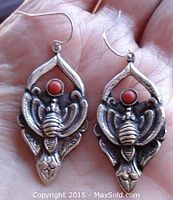 Front view of the pair of silver earrings with bug motifs and round coral stones set in the center.