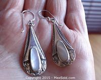 Full view of both earrings held in hand showing size, silver hooks, etched design and mother of pearl stones.