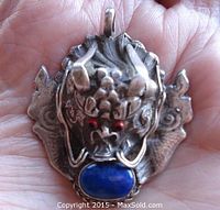 Front close-up showing detailed carved silver dragon's head with red and black eye stones holding oval lapis lazuli cabochon.