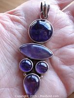 Front view of sterling silver pendant showing five amethyst stones in different shapes held in hand to display size and design.