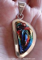 Front view of the sterling silver pendant featuring vibrant dichroic glass with multi-colored abstract design held in a hand for scale.