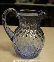 Front side view showing the diamond quilt pattern on the blue glass pitcher with twisted handle and pouring spout.