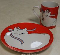 Plate and mug set placed on a beige surface showing the red background with a white cat and ribbon illustration.
