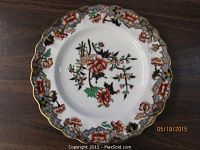 Single dessert plate showing floral Imari pattern with gold scalloped rim, set on wooden surface