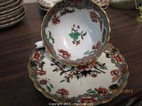 Close-up showing porcelain cup and saucer with Imari pattern; scalloped edges with gold trim, decorative floral design in red, green, black