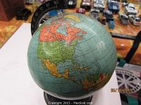Photo showing the vintage world globe with visible North America and surrounding areas, mounted on a metal stand with a numbered meridian ring.