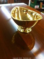 Gold glazed bonbon dish with reflective surface shown side angle on wooden table.