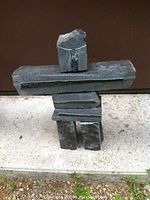 Front view of traditional Inuit style Inukshuk made from balanced solid granite pieces, placed on a concrete surface with a brown background.