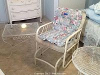 Glider style lawn chair with floral cushioned seating alongside square glass top table with white metal frame and decorative scrollwork.