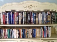 Two bookshelf shelves filled with hardcover books showing titles and authors on their spines, arranged side by side.