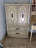 Full front view of cream-colored dresser with two ornate doors and two drawers beneath. Shows overall structure and hardware.