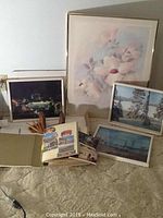 Four framed prints with various scenes and floral art, a postcard album open to show colorful postcards, and two wooden bookends.