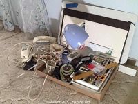 Image showing two desk telephones, desk lamp, lighted magnifying glass and other office items in a box on carpeted floor.