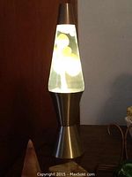 Lava lamp turned on and illuminated showing white wax blobs floating in clear liquid inside metallic base lamp.