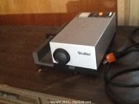 Rollei P350A slide projector showing front lens and power cord with orange plug on wooden surface.